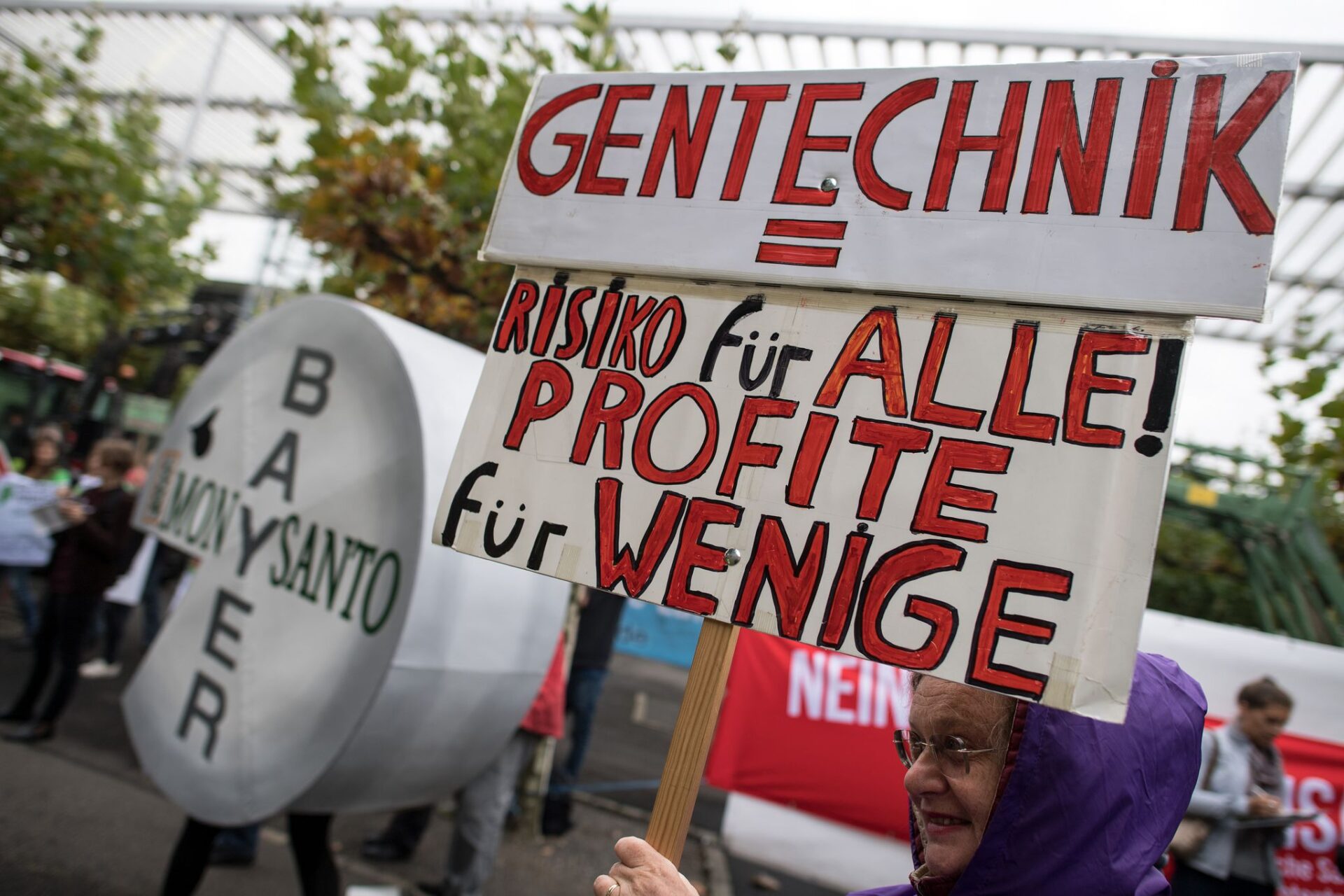 Das Bild zeigt einen Protest gegen Gentechnik. Die Protestierenden tragen Plakate, auf denen "Gentechnik = Risiko für Alle, Profite für Wenige" steht.