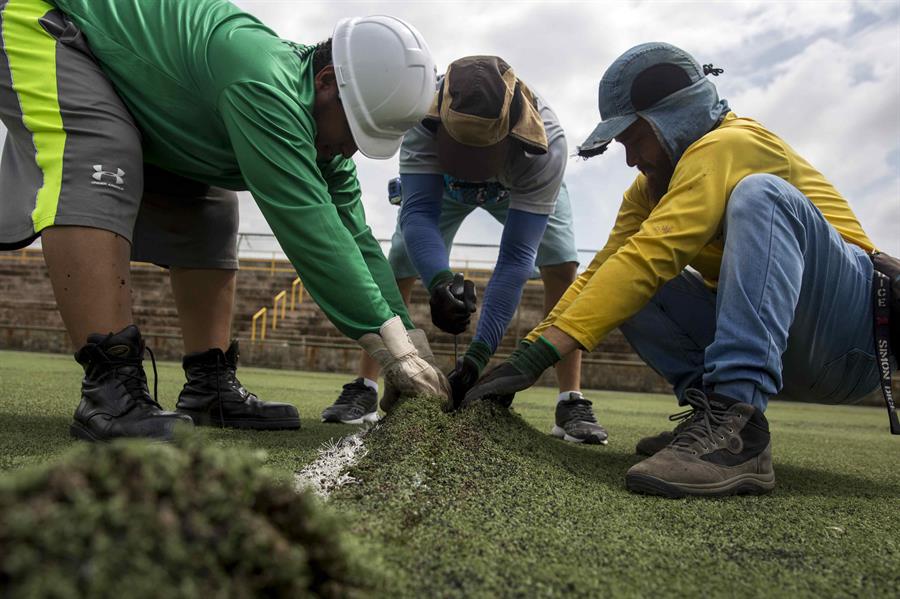 Varios trabajadores despegan la grama artificial en un estadio de fútbol. EFE/Jorge Torres.